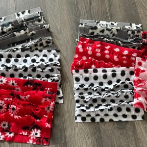 May include: A collection of fleece mats in various patterns. Designs include black and white polka dots, red with white daisies, and gray with black spots. The mats are arranged in stacks, showcasing their ruffled edges.