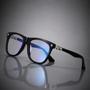 May include: Black-framed spectacles featuring silver-toned metal accents on the hinges and temples. The frames have a classic rectangular shape with clear lenses that exhibit a blue light-filtering tint. The temples display intricate silver detailing.