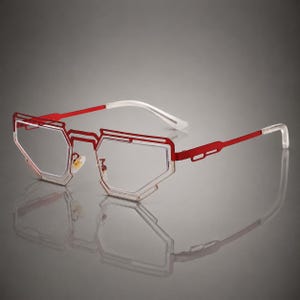 May include: Eyeglasses featuring a geometric, angular red metal frame with a cutout design. The lenses are clear and rimless within the frame structure. The temples are red metal with white translucent tips and adjustable gold-tone nose pads.