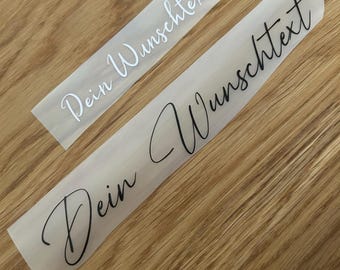Könnte beinhalten: Zwei selbstklebende Vinyl-Aufkleber auf einer transparenten Trägerfolie, die jeweils den deutschen Text "Dein Wunschtext" in einer schwarzen Schreibschrift zeigen. Die Aufkleber sind rechteckig und zeigen denselben individuellen Schriftzug.