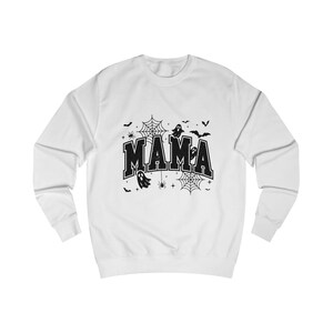 May include: A white long-sleeve crewneck sweatshirt featuring a black graphic print on the chest. The design displays the word MAMA in a bold collegiate font, surrounded by black illustrations of ghosts, spiderwebs, spiders, bats, and stars.