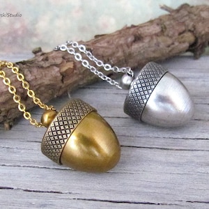 May include: Two acorn pendant necklaces. One has a gold-colored acorn pendant with a matching chain, and the other has a silver-colored acorn pendant with a silver chain. The acorn caps have a textured diamond pattern.