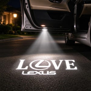 Puede incluir: Una puerta de coche está abierta por la noche, proyectando una luz blanca brillante sobre el asfalto oscuro. La luz forma un logotipo gráfico en el suelo que muestra la palabra LOVE con el emblema de Lexus como la letra O, seguido de LEXUS.