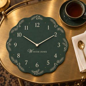 May include: A round, scalloped-edge wall clock with a dark green face, white numerals, and thin white hands. The clock features white line-art illustrations of pine branches and berries around the perimeter, with the text "WINTER HOME" printed in white.