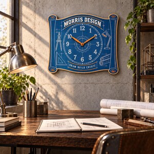 May include: A rectangular wall clock shaped like a scroll with a blue blueprint background. It features white numbers, orange hands, and illustrations of a compass, lamp, and triangle. The text reads MORRIS DESIGN and DRAW BUILD CREATE.