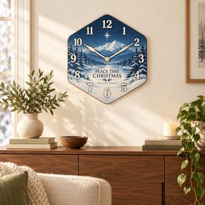 May include: A hexagonal wall clock featuring a winter landscape with snow-covered mountains, pine trees, and a starry sky. The clock face displays the text PEACE THIS CHRISTMAS and THE KING FAMILY, with white numbers and gold-toned hands.