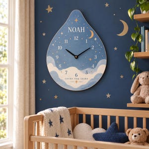 May include: A teardrop-shaped wall clock with a blue background featuring white clouds, gold stars, and a crescent moon. The clock face displays the name NOAH, numbers 1 through 12, and the text COUNT THE STARS with two black clock hands.