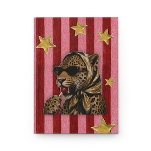 May include: A rectangular notebook featuring a leopard wearing a patterned headscarf and black sunglasses while holding a red lollipop. The background consists of vertical pink and dark red stripes decorated with several gold-coloured stars.