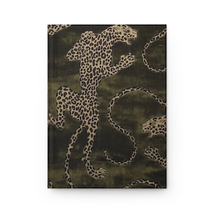 Puede incluir: Un diario de tapa dura con un fondo verde oliva oscuro y un patrón repetitivo de leopardos de color dorado en varias poses. Los leopardos están representados con manchas negras detalladas y bocas abiertas, creando un diseño audaz.