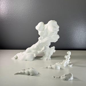 Puede incluir: Una colección de cuatro esculturas abstractas blancas con acabado mate, que presentan formas orgánicas, fluidas y similares a nubes. La pieza más grande es prominente, mientras que tres elementos escultóricos más pequeños se disponen delante.