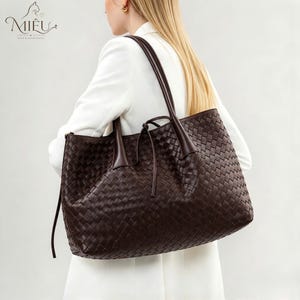May include: A dark brown tote bag featuring an intricate woven leather pattern, two long shoulder straps, and a thin drawstring tie closure at the top centre. The bag is displayed against a plain background with the Miêu logo in the corner.
