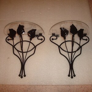 May include: A pair of black metal wall mounted shelves with a clear acrylic top. Each shelf features three decorative leaf-shaped hooks.
