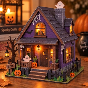 May include: A miniature purple house with a dark grey roof, a chimney topped with a ghost, and illuminated windows. The exterior features spider webs, bats, a crescent moon on the door, and a sign reading BOO! with small orange jack-o'-lanterns.