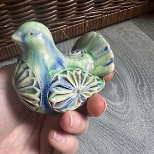 Könnte beinhalten: Eine Keramik-Vogelfigur mit einer Craquelé-Glasur in hellgrünen und blauen Farbtönen. Der Körper ist mit geschnitzten, fächerförmigen Mustern an den Flügeln und am Schwanz verziert, die eine glänzende Textur und durchgehend feine Details aufweisen.