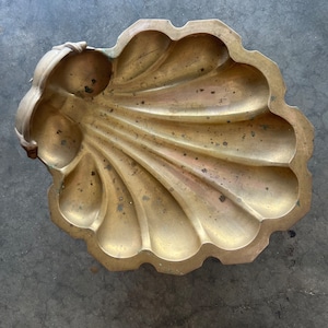 May include: A brass shell-shaped dish with a decorative handle. The dish is a vintage style and has a worn, antique look.