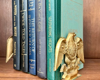 May include: Gold eagle bookends holding up a set of five books. The books are all different colors and have titles like "The Da Vinci Code" and "Wuthering Heights".