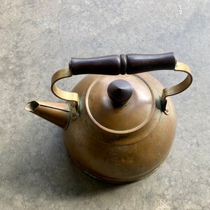May include: A vintage copper kettle with a wooden handle and brass accents. The kettle has a tarnished finish and is in good condition.