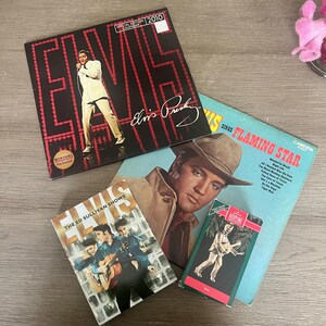 May include: A selection of Elvis Presley collectibles, including a 2010 calendar, vinyl records, and a Hallmark ornament. The calendar shows Elvis on stage. The records feature album art of Elvis in different poses.