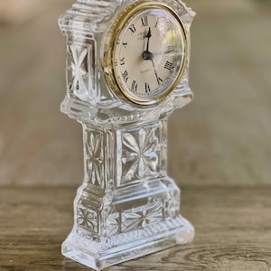 Puede incluir: Un reloj de cristal con una esfera dorada y números romanos. El reloj dice "Crystal Legend Quartz".