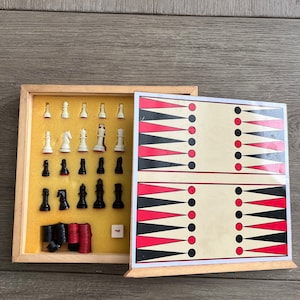 Puede incluir: Una caja de madera que contiene un juego de ajedrez y un tablero de backgammon. Las piezas de ajedrez son blancas y negras, y el tablero de backgammon es rojo, negro y blanco.