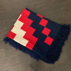 K&ouml;nnte beinhalten: Eine rot-wei&szlig;-blaue karierte Wolldecke mit Fransen. Die Decke ist aus einem weichen, gewebten Stoff.