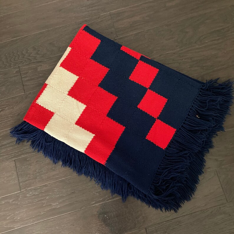 K&ouml;nnte beinhalten: Eine rot-wei&szlig;-blaue karierte Wolldecke mit Fransen. Die Decke ist aus einem weichen, gewebten Stoff.