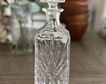 May include: A clear glass decanter with a square base and a diamond-shaped pattern. The decanter has a square stopper.