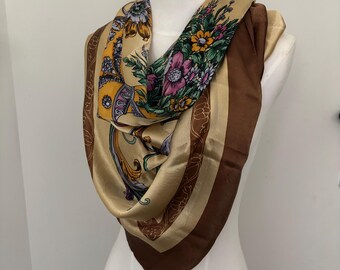 May include: A square silk scarf with a floral and ornamental design. The scarf features a tan background with brown borders and a central panel with colorful flowers and decorative elements. The scarf is draped over a mannequin.