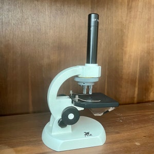 Vintage Studentenmikroskop Metallkörper Weiß & Schwarz K12-Mikroskop mit Prisma auf Unterseite Vintage Arbeitsgeräte