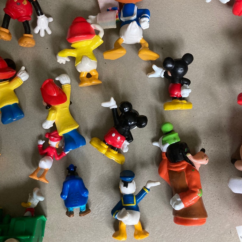 May include: A collection of vintage Disney character figurines, including Mickey Mouse, Donald Duck, Goofy, and others. The figurines are made of plastic and are painted in bright colors.