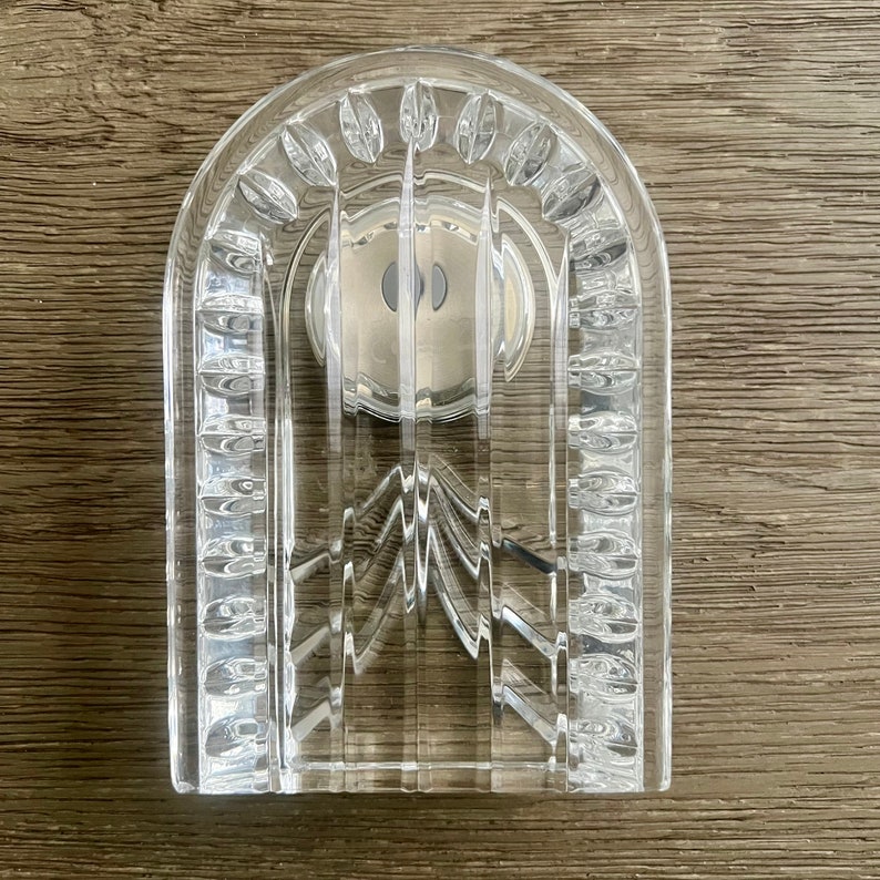 May include: A clear crystal arch-shaped soap dish with a decorative design. The dish has a silver-colored metal insert in the center.