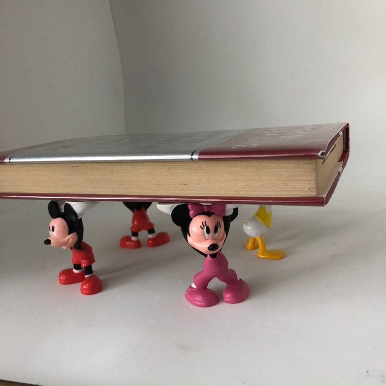K&ouml;nnte beinhalten: Vier bunte Plastikfiguren, die ein Buch hochhalten. Die Figuren sind Mickey Mouse, Minnie Mouse, Donald Duck und Goofy. Das Buch ist rot und hat einen wei&szlig;en R&uuml;cken.