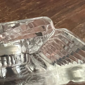 May include: A clear glass bowl with a textured, faceted design. The bowl is made of thick glass and has a rounded shape.