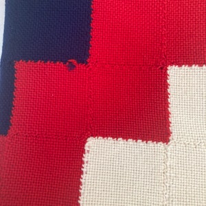 K&ouml;nnte beinhalten: Nahaufnahme eines gewebten Stoffes mit Patchwork-Muster. Der Stoff besteht aus Quadraten in Rot, Wei&szlig; und Dunkelblau.