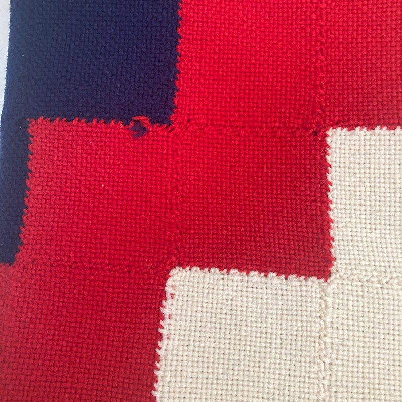 K&ouml;nnte beinhalten: Nahaufnahme eines gewebten Stoffes mit Patchwork-Muster. Der Stoff besteht aus Quadraten in Rot, Wei&szlig; und Dunkelblau.