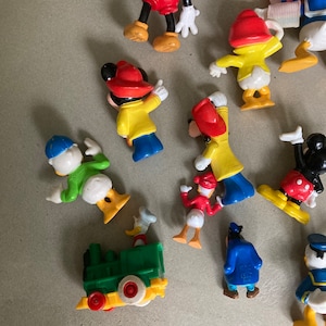 May include: A collection of vintage Disney character figurines, including Mickey Mouse, Donald Duck, and Goofy. The figurines are made of plastic and are painted in bright colors. They are in good condition and would be a great addition to any Disney collection.