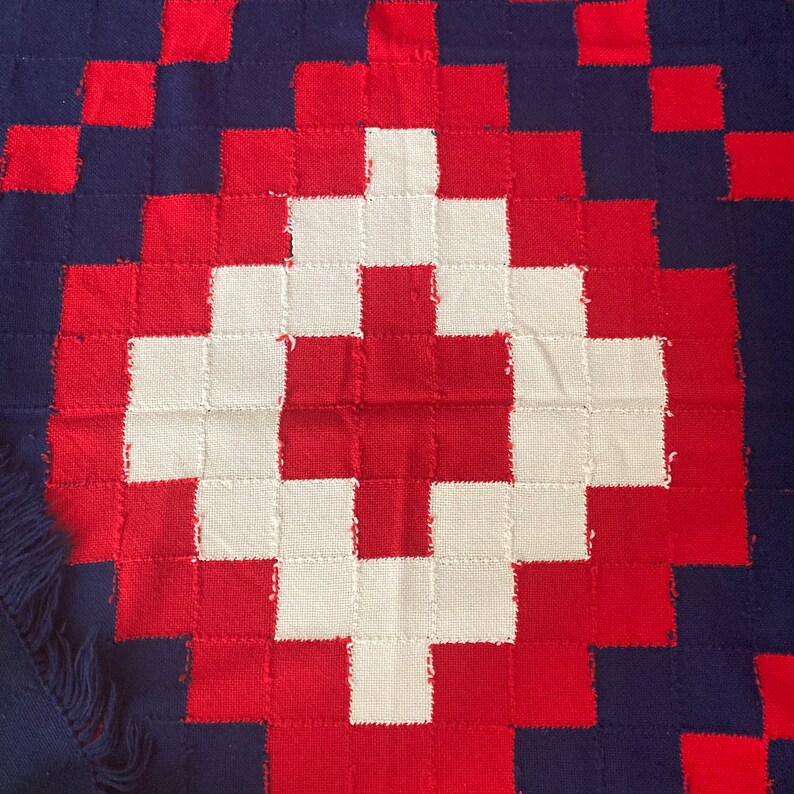 K&ouml;nnte beinhalten: Eine rot-wei&szlig;-blaue gewebte Decke mit einem gro&szlig;en wei&szlig;en Kreuz in der Mitte. Die Decke besteht aus Quadraten und hat einen Fransenrand.