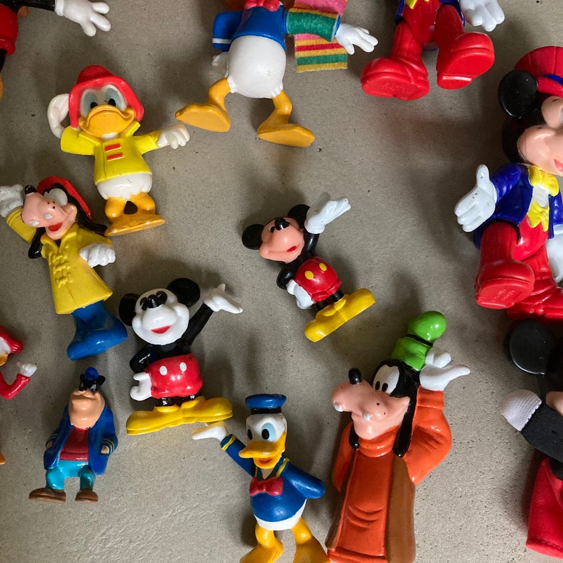 May include: A collection of vintage Disney character figurines, including Mickey Mouse, Donald Duck, Goofy, and Pluto. The figurines are made of plastic and are painted in bright colors. They are all in good condition and would make a great addition to any Disney fan's collection.