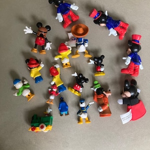 May include: A collection of 17 plastic figurines of various Disney characters, including Mickey Mouse, Donald Duck, Goofy, and Pluto. The figurines are in various poses and are painted in bright colors. The figurines are all about 2 inches tall.