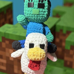 May include: Crocheted Minecraft-inspired plush toys. A green zombie figure with black hair and a blue shirt sits atop a white chicken with a yellow beak and red wattle. The toys are handmade and feature pixelated details.