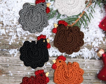 May include: Six crocheted chicken ornaments in different colors: white, gray, brown, black, orange, and red. The ornaments are on a wooden surface with white snow-like material.