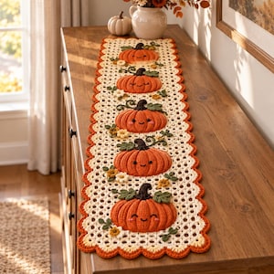 May include: A rectangular crochet table runner featuring a cream-colored openwork lace pattern with a scalloped orange border. Five three-dimensional orange pumpkins with dark brown stems, green leaves, and embroidered smiling faces are centered.