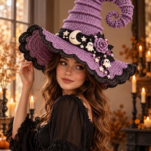 Puede incluir: Un sombrero de bruja de ganchillo morado con punta curvada y ala ancha con borde negro. El sombrero presenta una banda negra decorada con una luna creciente color crema, estrellas pequeñas, dos figuras de fantasmas blancos, una rosa y perlas.