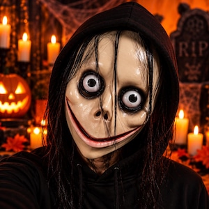 May include: A full-head mask featuring a pale, smooth face with extremely large, round, black-and-white eyes and a wide, thin, red-lipped mouth stretched into a grin. The mask has long, thin, dark hair strands and an attached black hooded sweatshirt.