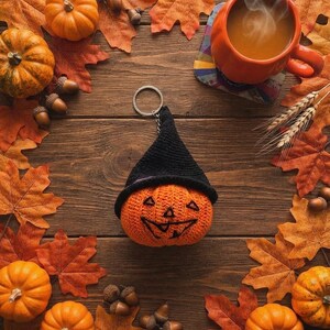 Peut inclure: Un porte-clés citrouille orange crocheté portant un chapeau pointu noir. La citrouille présente un visage de jack-o'-lantern noir brodé avec des yeux triangulaires et une bouche dentelée. Un anneau en métal argenté est fixé au chapeau.