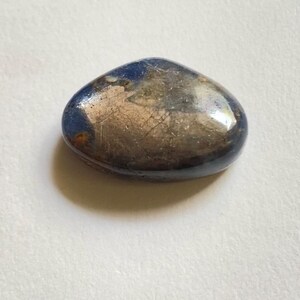 May include: A polished, smooth, oval-shaped stone featuring a deep blue colour on the edges that transitions into a metallic, reflective silver-grey centre with visible fine surface cracks and natural mineral inclusions across the top surface.