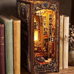 Puede incluir: Un inserto de madera para estantería que presenta una escena de biblioteca en miniatura iluminada con filigrana dorada, un reloj en la parte superior y el texto Spring and Autumn in the Temple en el lateral, creando un efecto de diorama 3D.