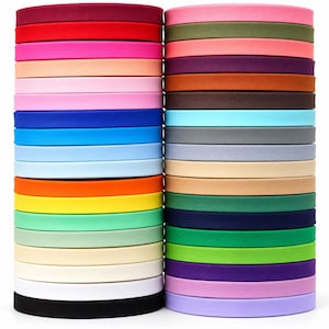 May include: Two vertical stacks of circular fabric bias tape rolls in a wide variety of solid colors including red, pink, orange, yellow, green, blue, purple, black, white, and various neutral shades, arranged in a neat, organized column formation.