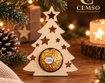 Può includere: Un addobbo per albero di Natale in legno chiaro con diversi intagli a forma di stella e un'apertura circolare al centro che contiene un cioccolatino rotondo avvolto in carta dorata con etichetta bianca Ferrero Rocher.