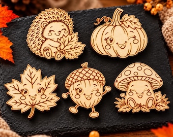 Può includere: Cinque sagome in legno con personaggi dei cartoni animati incisi: un riccio che tiene una foglia, una zucca che fa l'occhiolino, una foglia d'acero sorridente, una ghianda che fa l'occhiolino e un fungo su foglie.